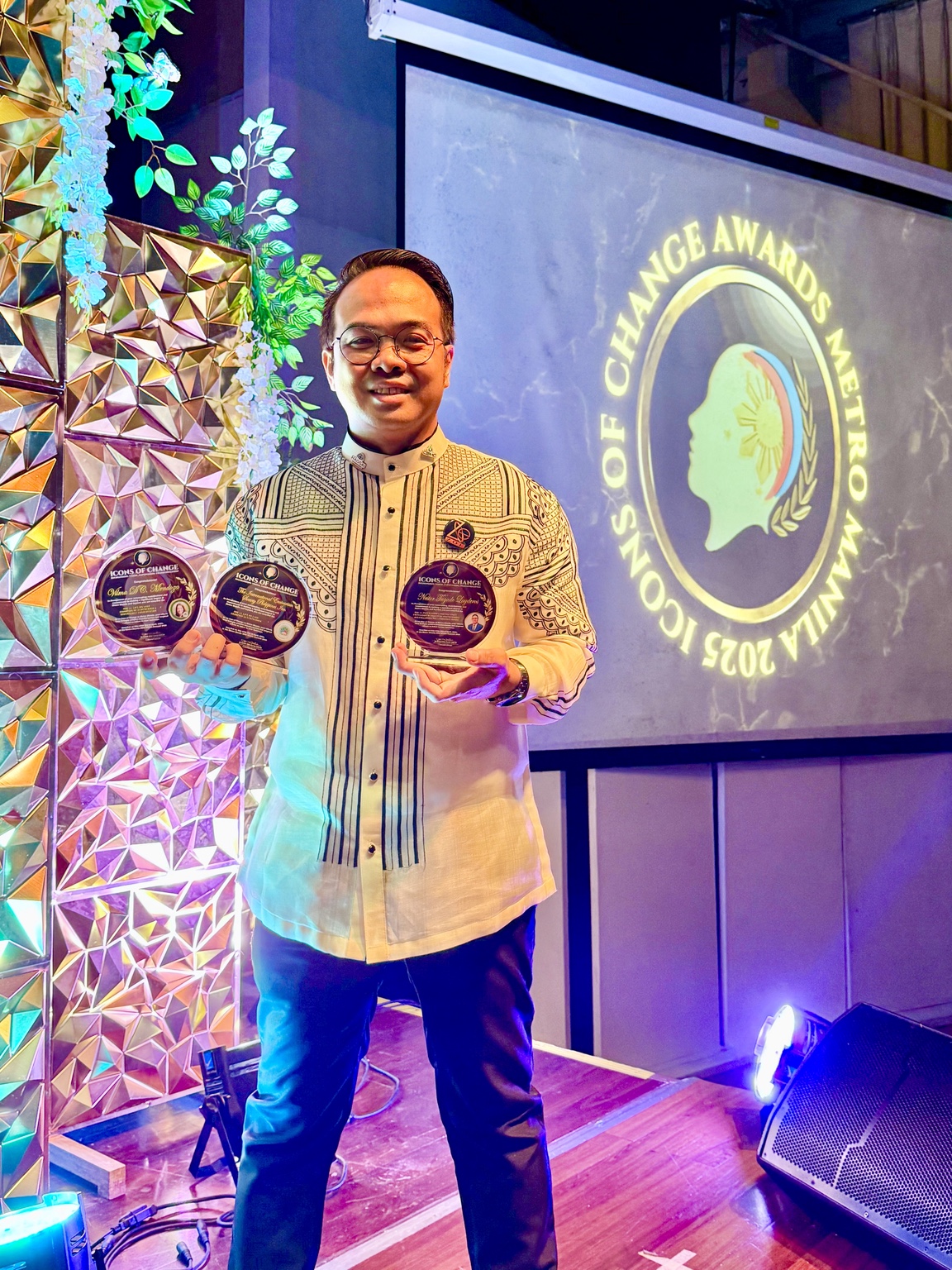 Sir Next holding two Icons of Change plaques beside the event stage