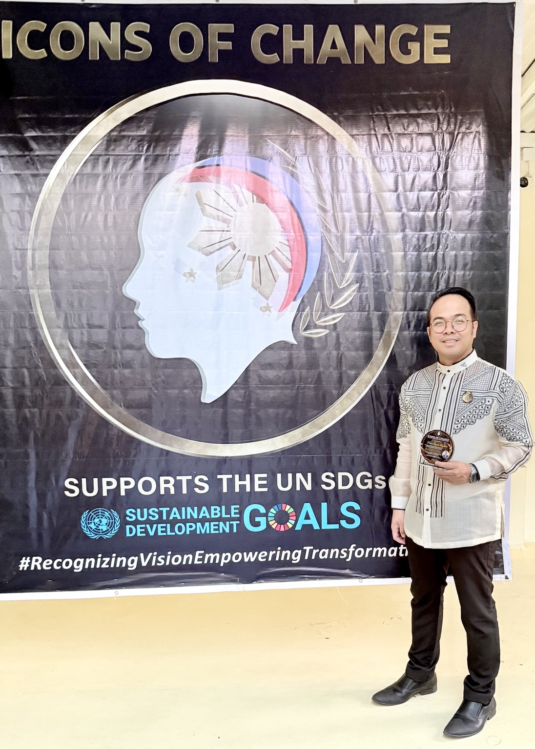 Sir Next holding his award beside the Icons of Change event banner